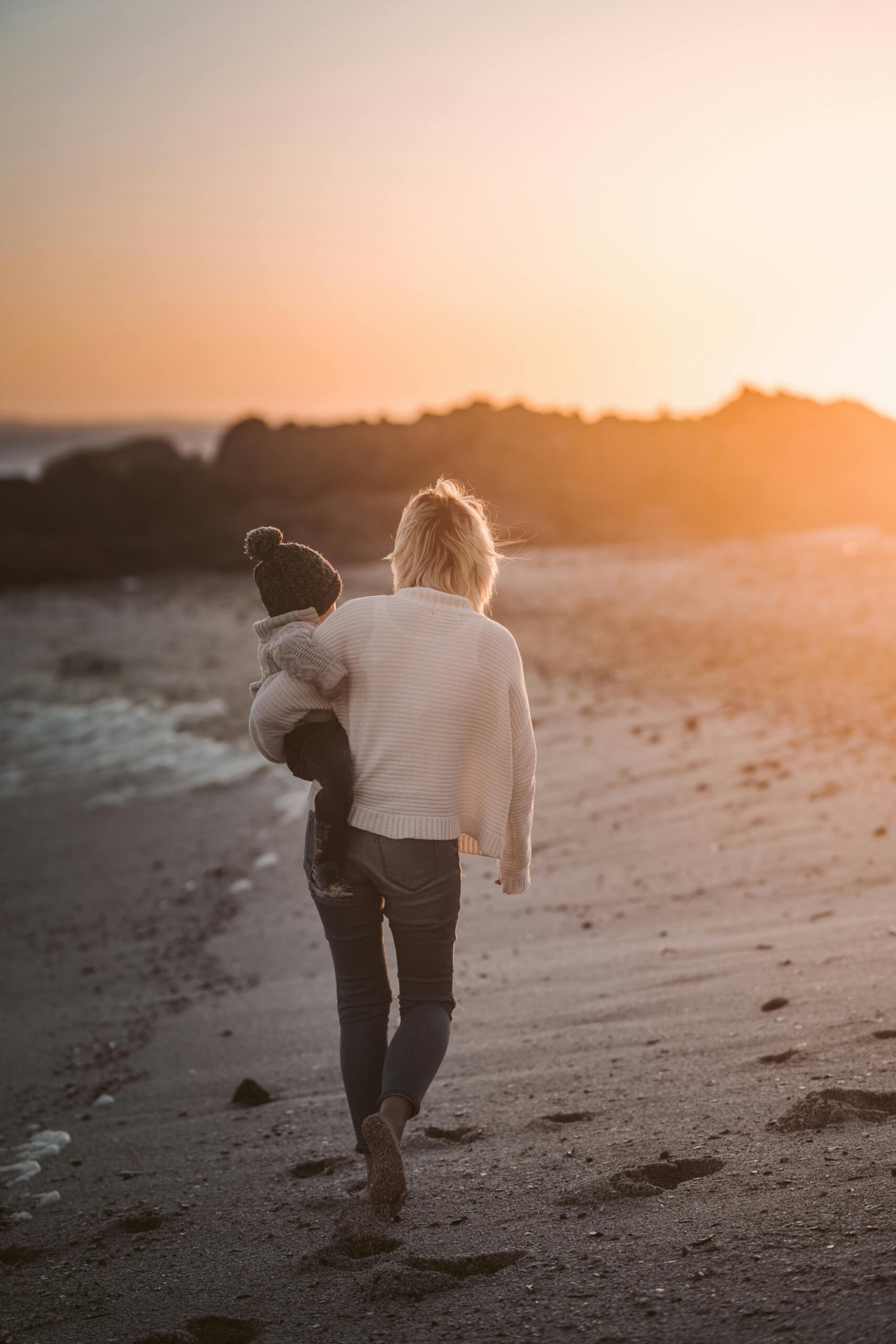Femme de dos portant un enfant sur la plage, illustration pension alimentaire et prestation compensatoire