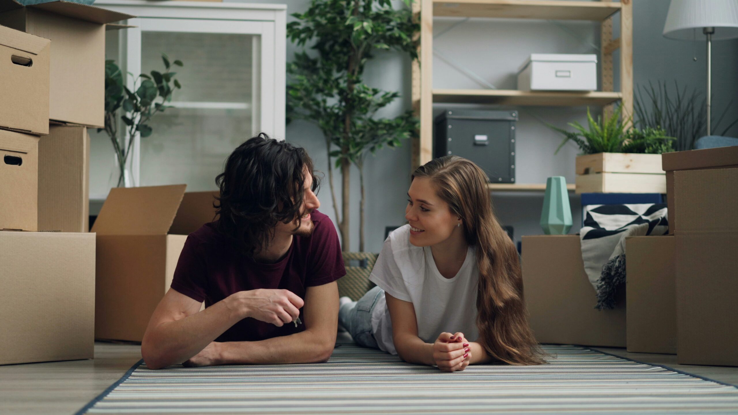 Jeune couple allongé au sol, clés en main, cartons de déménagement ; illustration d’un article sur la caution et le dépôt de garantie en location.